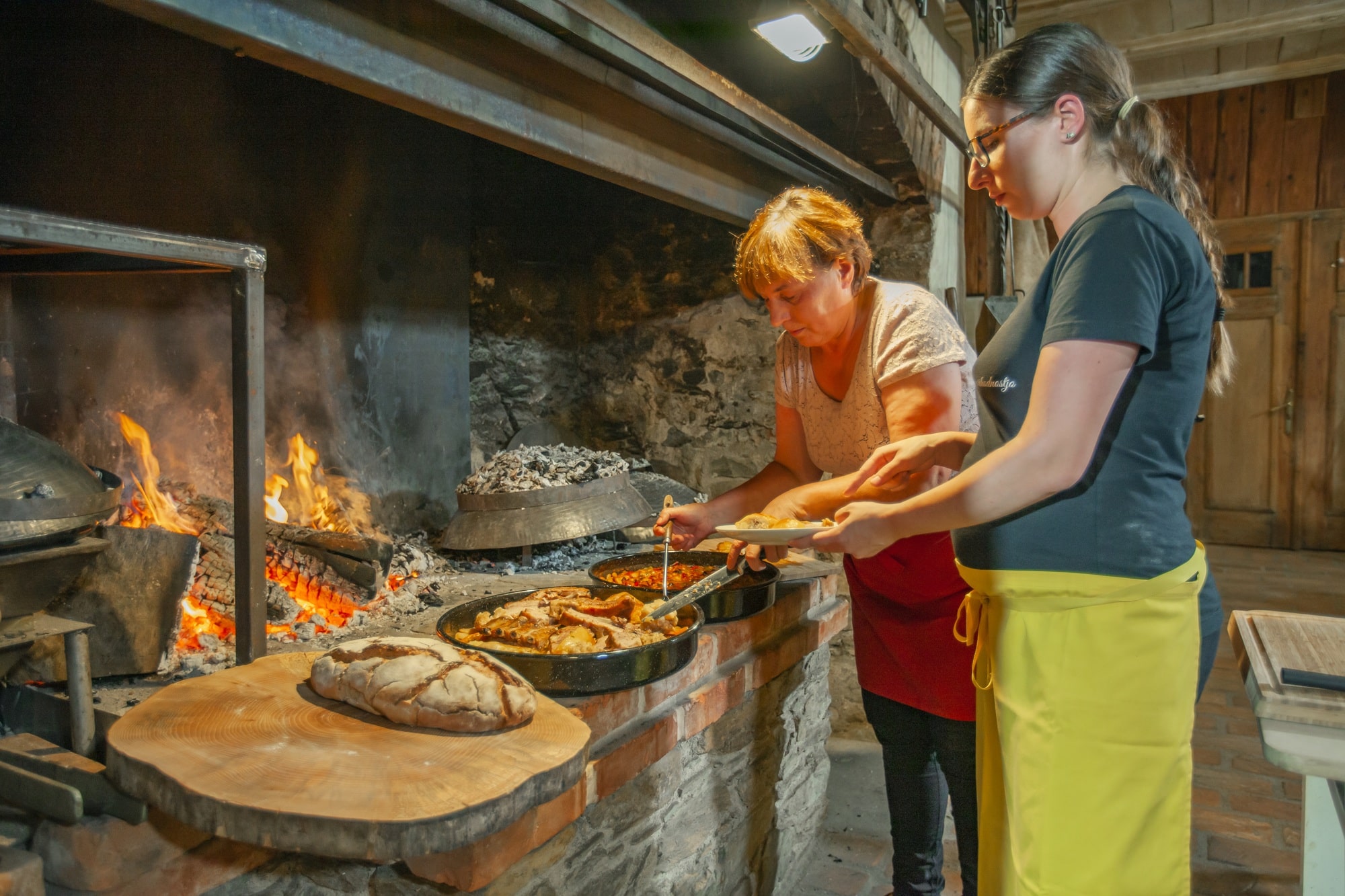 Two women near the fire baking bread and preparing traditional Slovenian food made of pig ribs